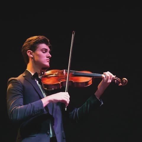 A violist performing on stage under dramatic lighting